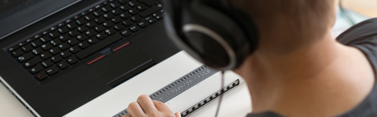 Visually impaired working on computer with assistive technology; braille display and screen reader.